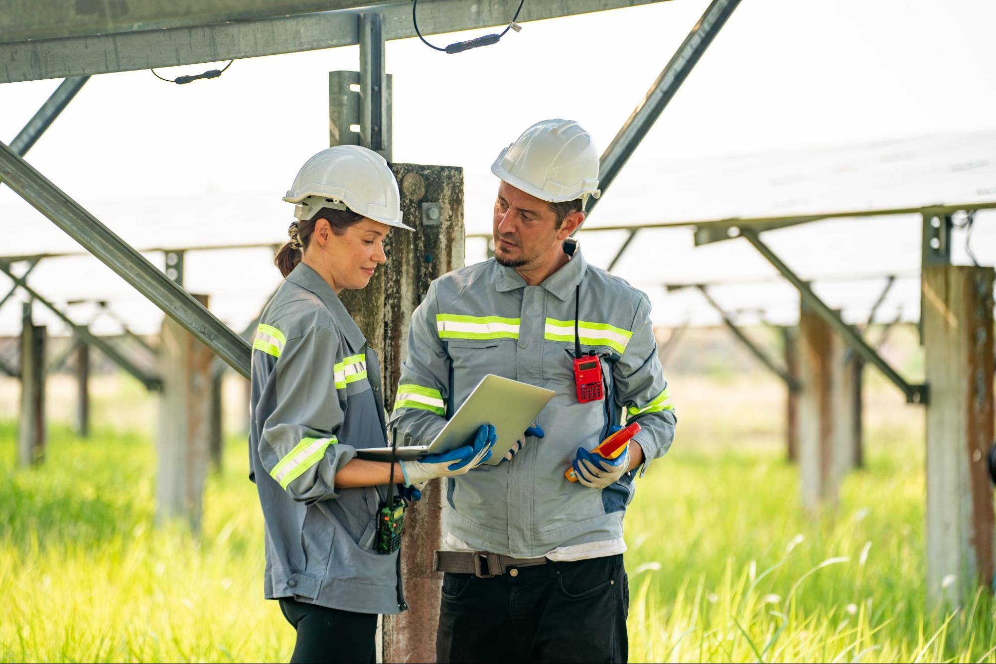 A man and a woman wearing uniforms are looking at a laptop in the field.