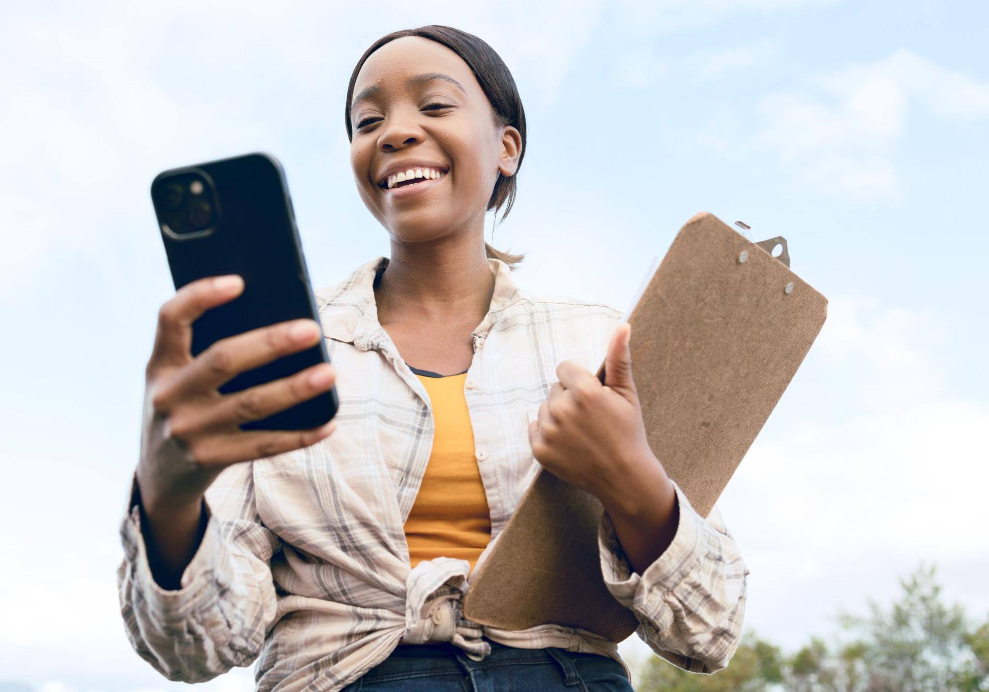 Smiling woman holding a clipboard and using a phone. 