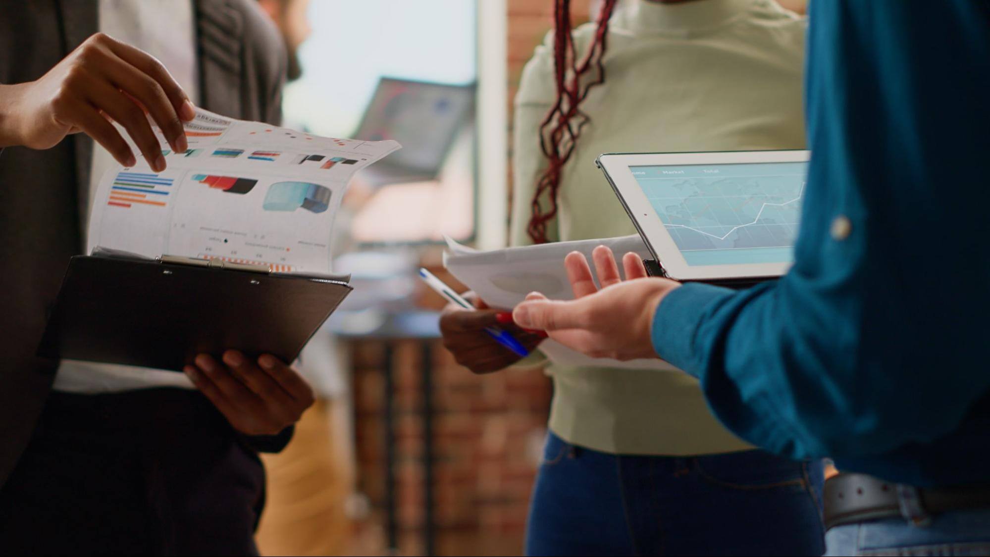  Three people using iPads and looking at charts printed on pieces of paper. 