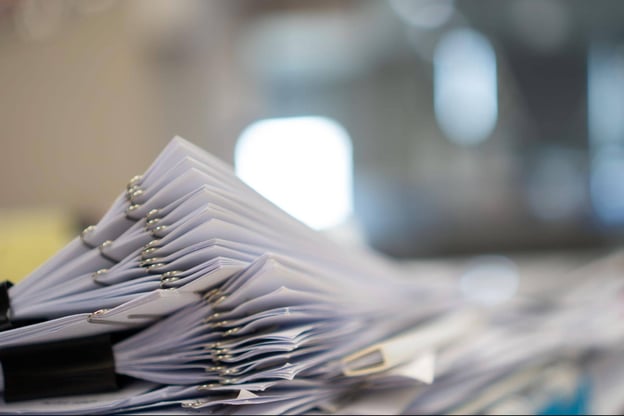 A stack of papers representing numerous forms waiting to be filled, all piled up on a table, symbolizing a busy workload and administrative burden.